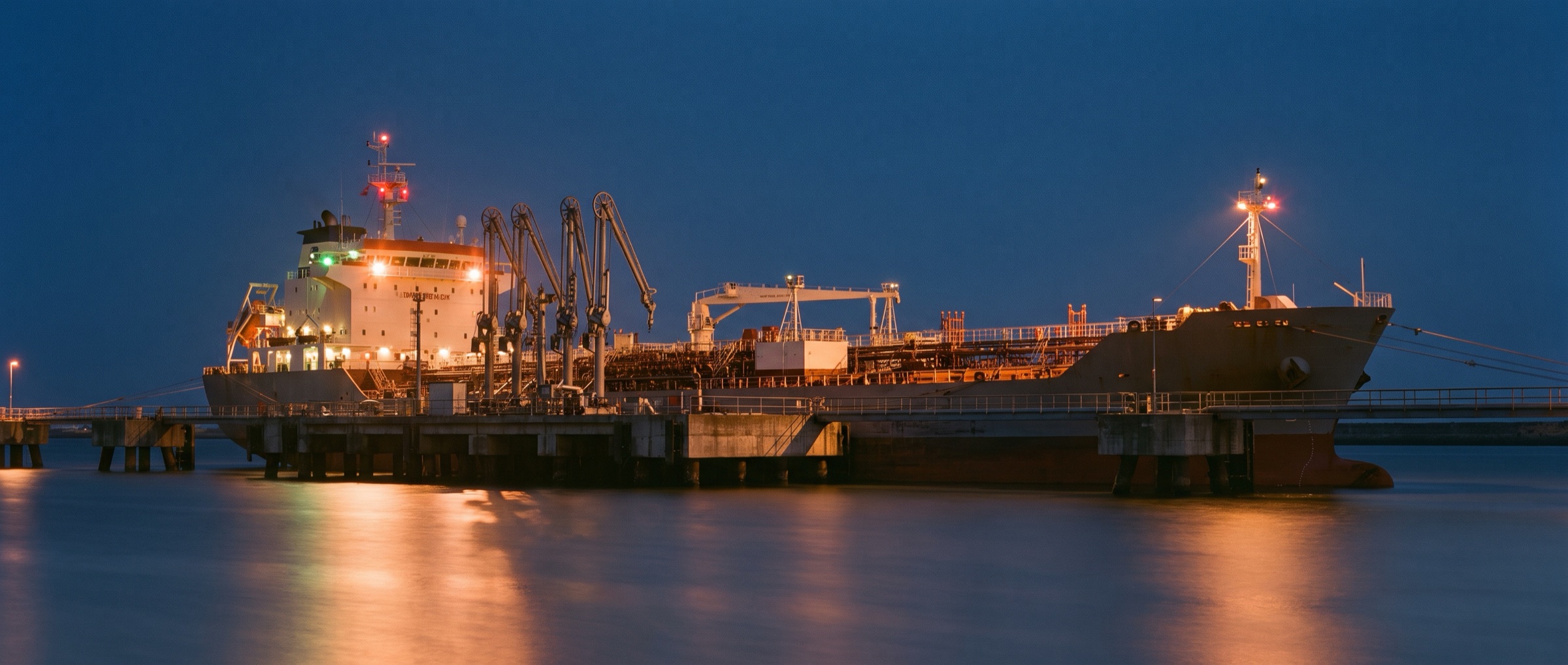 Tanker at berth beside jetty loading arms at dusk